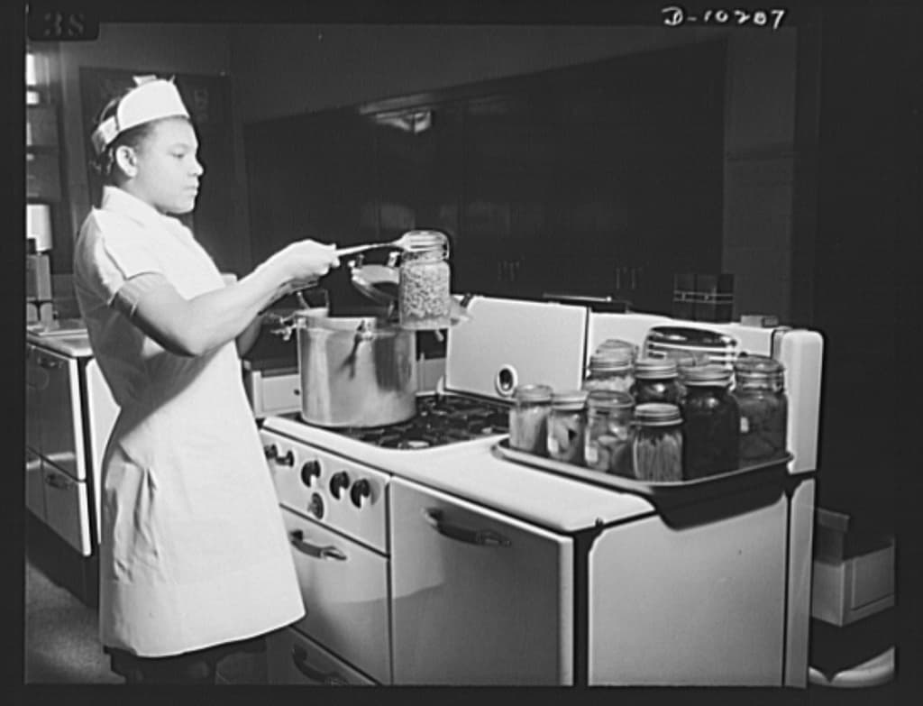 Miss Laura Russell removing a jar of canned string beans from a pressure cooker in 1943